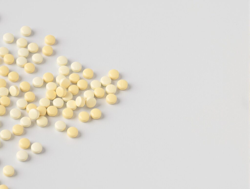 Many yellow pills are spilled on a white background